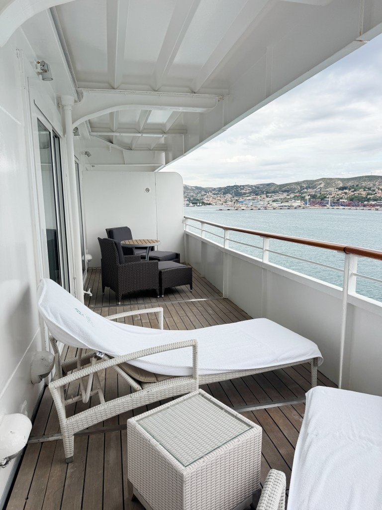 A large cruise ship veranda with sunloungers and a table and chairs.
