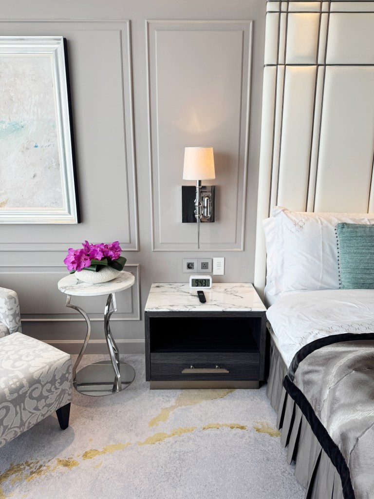 A bedside photo with pink flowers on the table, an armchair and a bed.