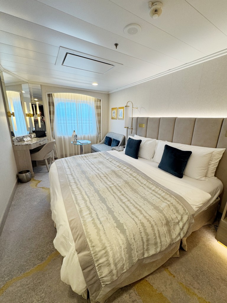 A Large double bed with a window to the ocean in the distance.