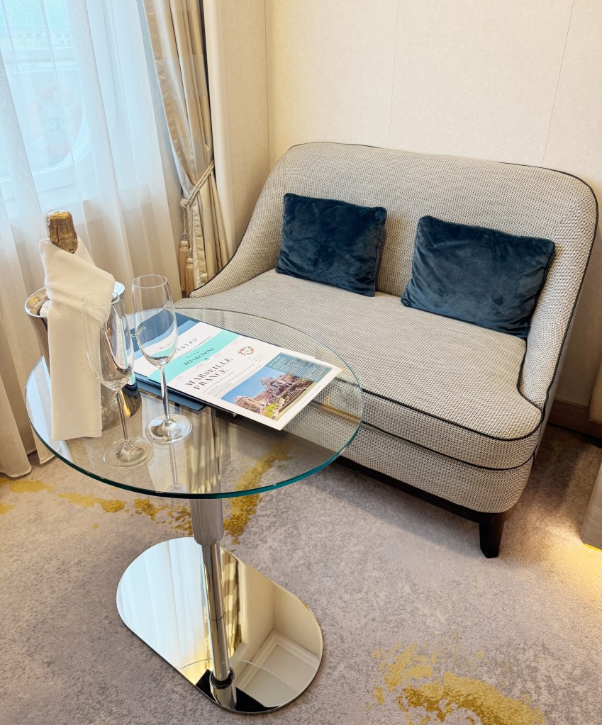 A sofa alongside a window, with a small coffee table and a bottle of Champagne with two glasses