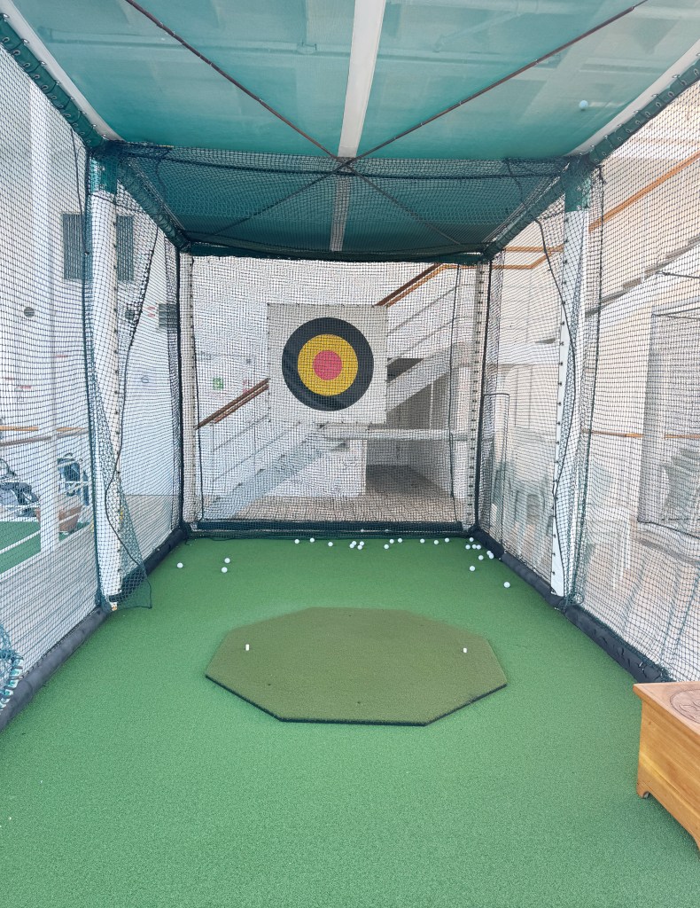 A Gold driving net with lots of golf balls on the floor.