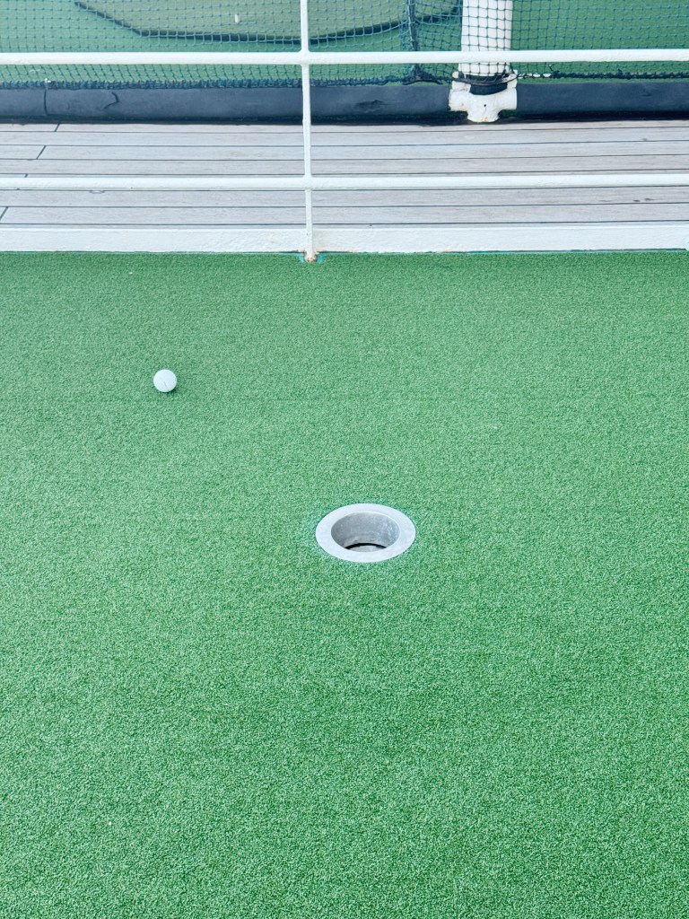 A putting green with a hole and one golf ball
