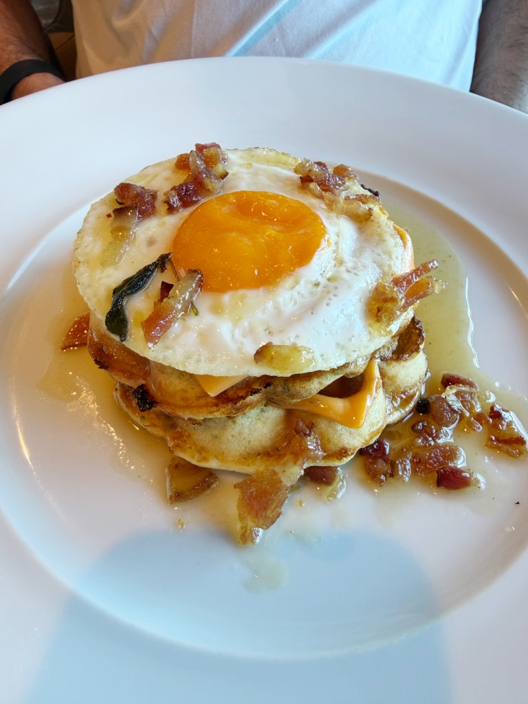 A fried egg on top of a stack of pancakes on a plate