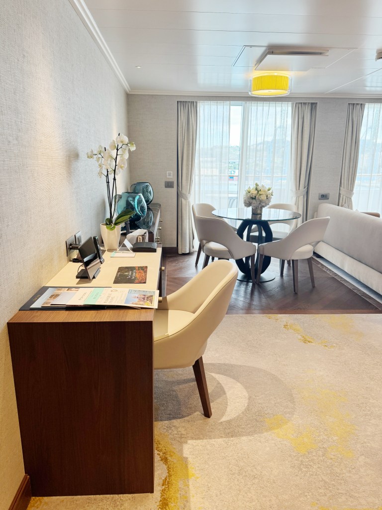 A desk in the foreground with a dining table and veranda door in the background