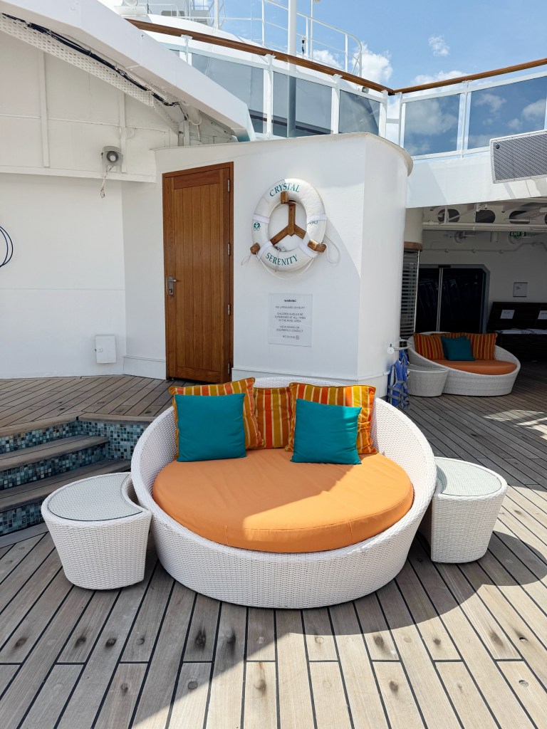 A orange round sunlounger for two with a white frame and turquoise cushions.