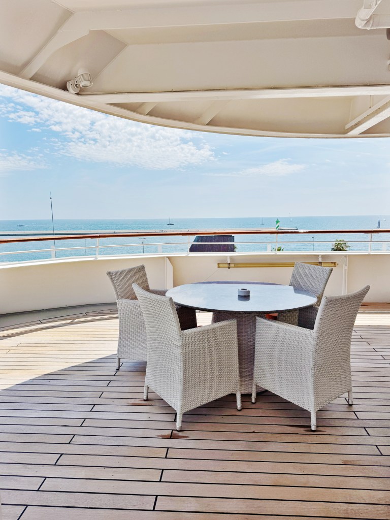 A white table and chairs on an open deck with a sea view behind.