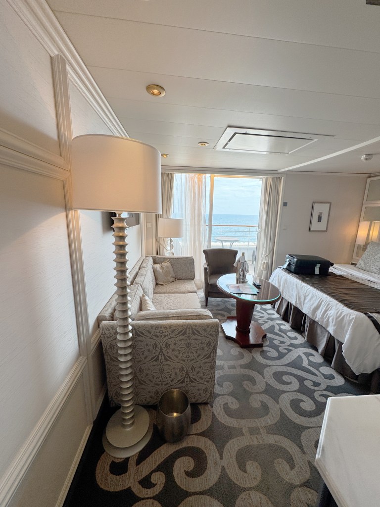 A view of the suite from the entrance corridor, showing bed, seating area and balcony door in the distance.