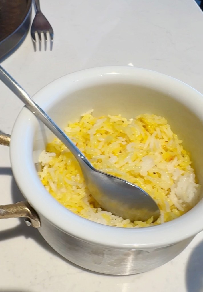 A bowl of yellow and white rice with a metal spoon resting inside.