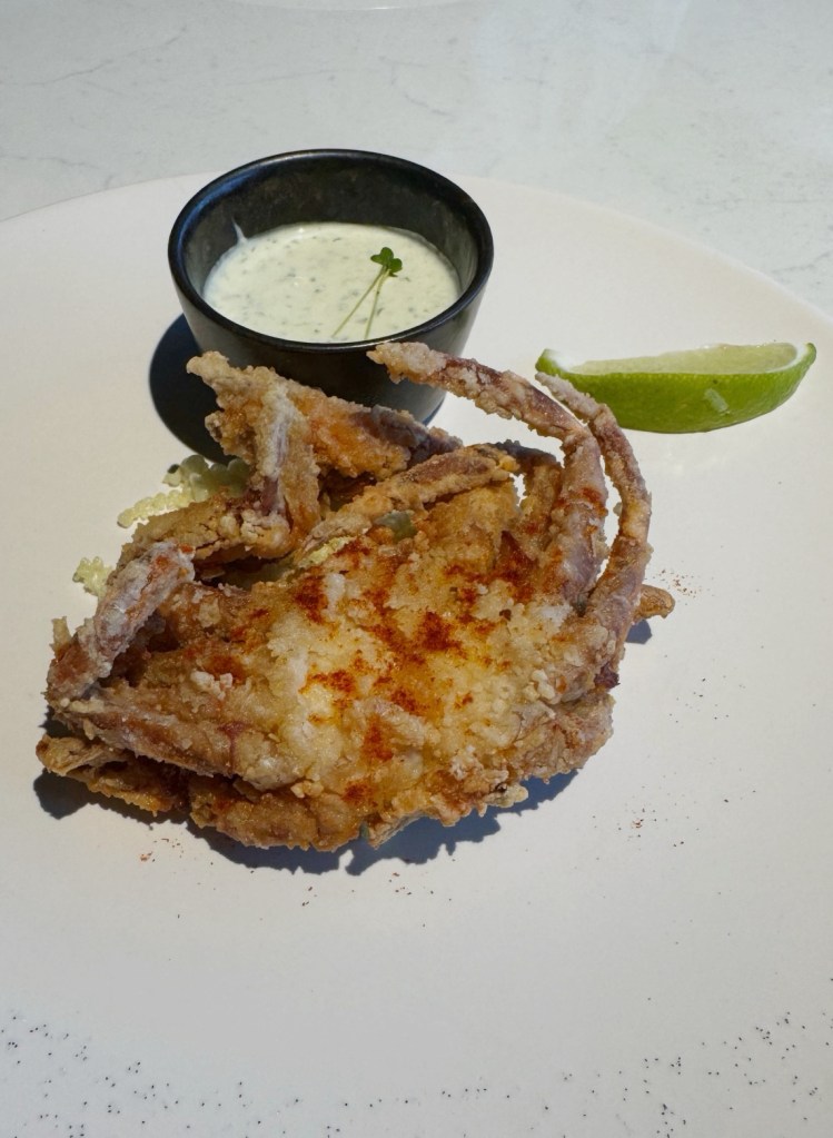 Fried soft-shell crab served with a small bowl of dipping sauce and a lime wedge on a white plate.