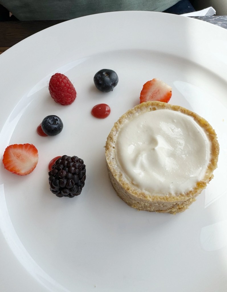 A vanilla cheesecake with a selection of berries places next to it on a white plate.