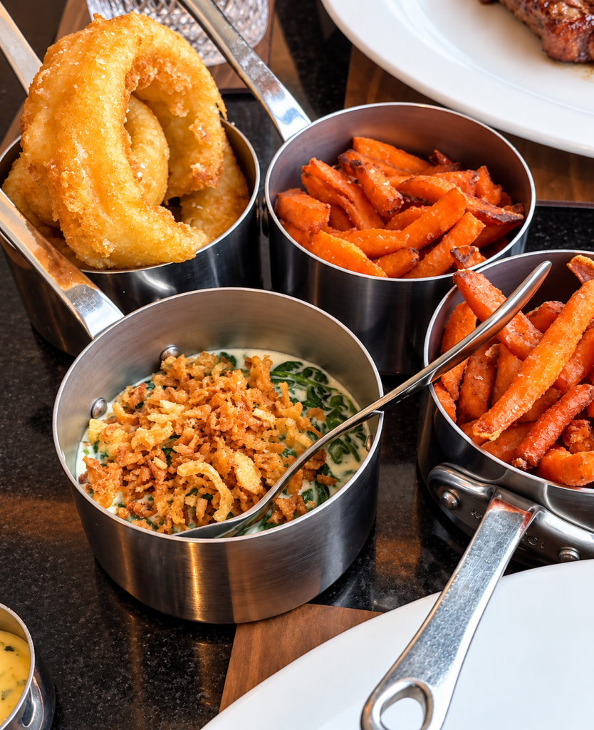 A dish of creamed spinach, onion rings and sweet potato fries.